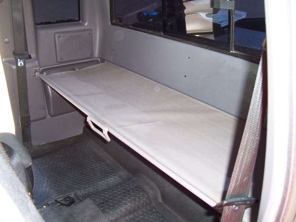 Interior of a truck cab showing a fold-down shelf above rubber floor mats and a seatbelt