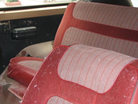 1986 Ford Bronco - The interior of the vehicle shows worn red seats with a striped pattern and a dusty door panel.