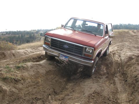 1986 Ford Bronco - A red Ford Bronco is shown off-roading on a dirt track with deep ruts.
