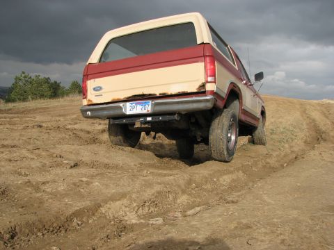 1986 Ford Bronco - This two-tone 1986 Ford Bronco navigates a challenging off-road terrain under a stormy sky.