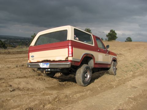 1986 Ford Bronco - Rear view of a 1986 Ford Bronco on a dirt trail under a cloudy sky.