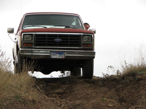 1986 Ford Bronco - A red pickup truck navigates a rough, off-road trail with dry grass on the sides.