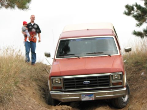 1986 Ford Bronco - Man holds baby while standing next to a red Ford Bronco on a dirt hill.