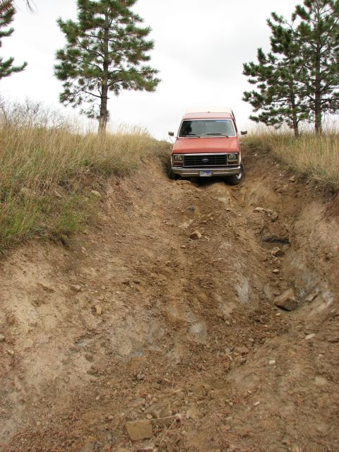 1986 Ford Bronco - A van navigates a challenging off-road trail, with steep inclines and loose dirt.