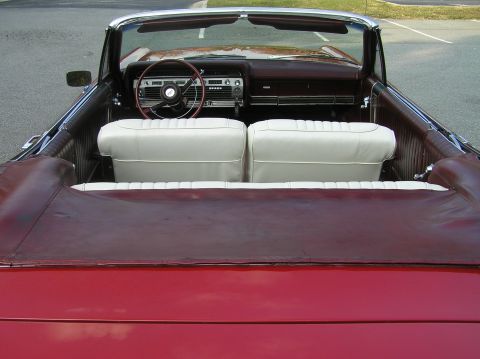1967 Ford Galaxie - The interior of a red convertible shows white seats and a dark dashboard with a steering wheel.