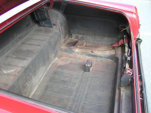 1967 Ford Galaxie - The trunk interior of a red 1967 Ford Galaxie shows signs of wear on the floor and side panels.