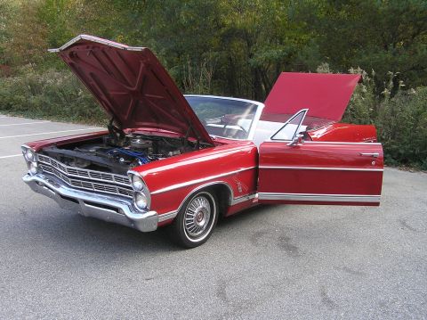 1967 Ford Galaxie - The front of a red convertible is shown with the hood and driver's door open, revealing the engine.