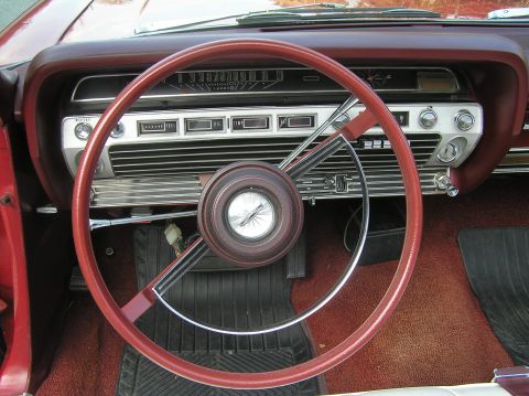 1967 Ford Galaxie - The dashboard features a horizontal speedometer and various controls, with a red steering wheel in the foreground.