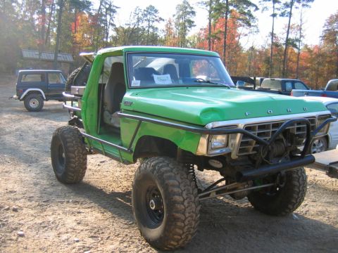1992 Ford Mustang - A modified green truck with off-road tires sits on a dirt lot, with other vehicles and trees in the background.