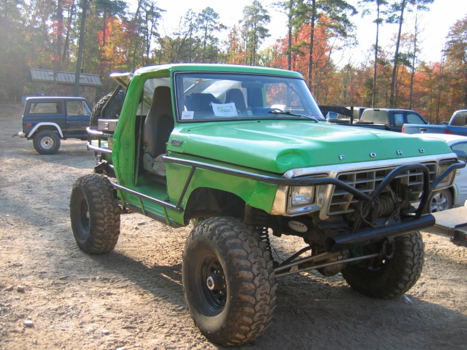 Green off-road truck with large tires and a winch, parked on dirt
