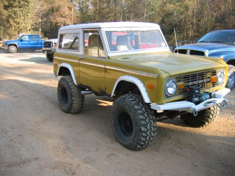 1992 Ford Mustang - Modified Ford Bronco with off-road tires parked on a dirt road, with other trucks in the background.