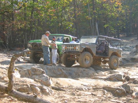 1992 Ford Mustang - Two off-road vehicles navigate a challenging rocky trail in a wooded area.
