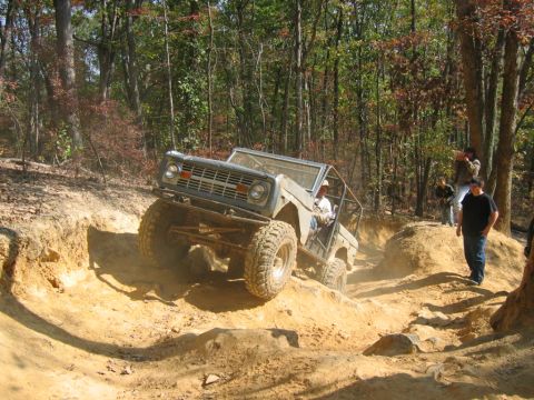 1992 Ford Mustang - A modified Ford Bronco navigates a challenging off-road trail with spectators watching.