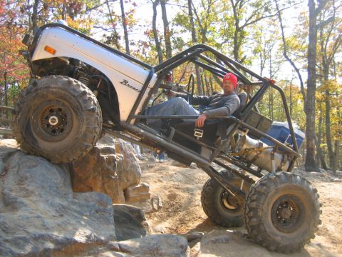 1992 Ford Mustang - A modified off-road vehicle, possibly a Bronco, navigates a rocky trail with a driver inside.