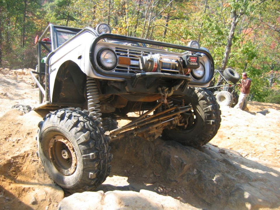 Modified Ford Bronco on rocks, winch on front bumper. Another vehicle and person in background
