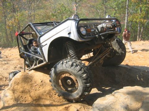 1992 Ford Mustang - Modified Ford Bronco navigates a rocky trail with a person inside and another person taking a photo in the background.