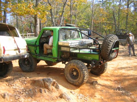 1992 Ford Mustang - A modified green pickup truck is parked on a dirt trail next to another vehicle, with trees and autumn foliage in the background.