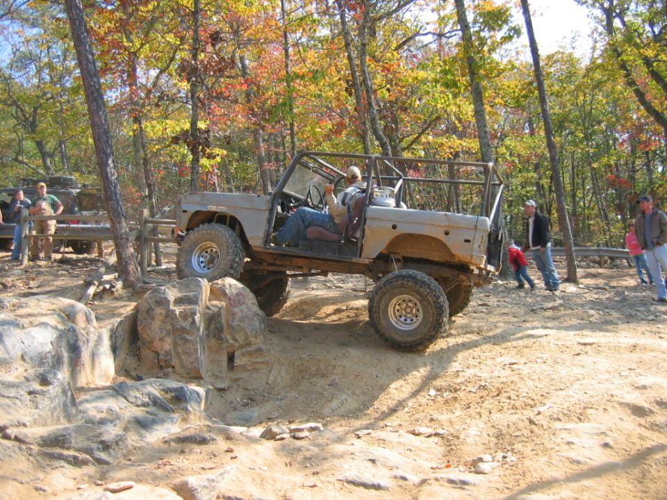 Tan Ford Bronco off-roading over rocks, driver visible, roll cage installed