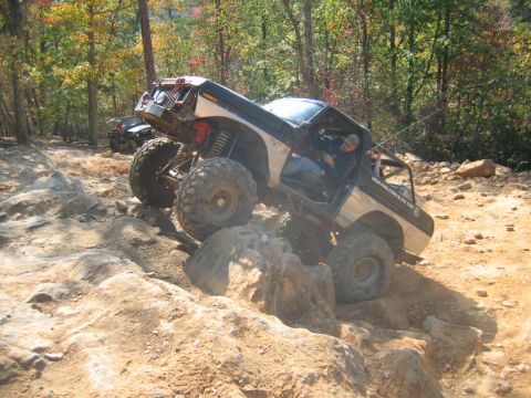 1992 Ford Mustang - A modified off-road vehicle navigates a challenging rocky terrain on a sunny day.