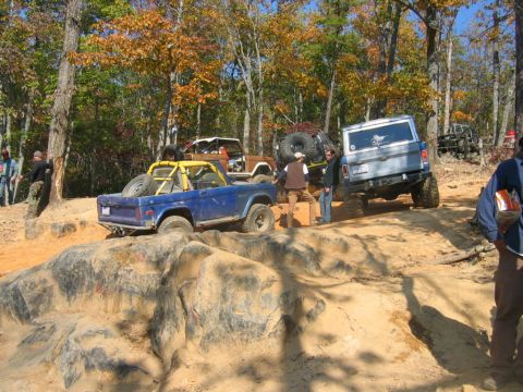 1992 Ford Mustang - Several Ford Broncos navigate a challenging off-road course with rocky obstacles and autumn foliage.