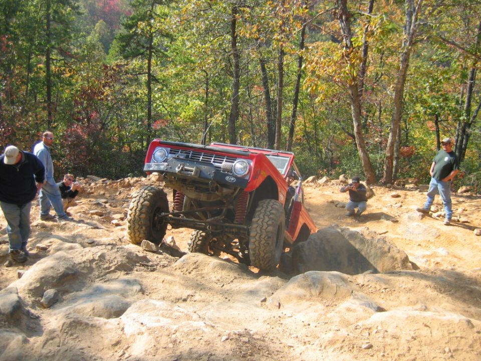 Red Bronco climbing over rocks on a trail, people watching
