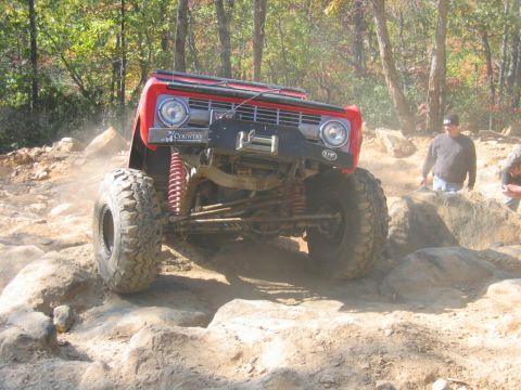 1992 Ford Mustang - A red off-road vehicle tackles a challenging rocky trail, kicking up dust.