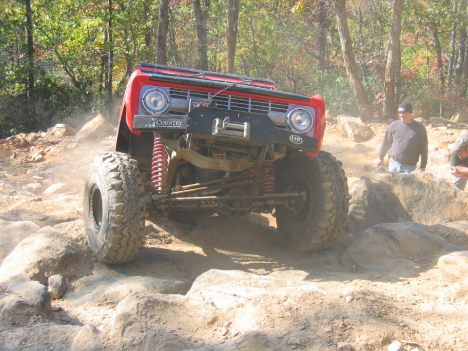 Red off-road vehicle with large tires navigating rocky terrain. Visible text on bumper reads 'COUNTRY'