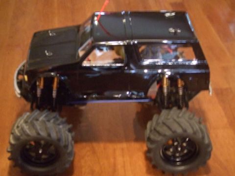 1995 Ford Mustang - A black remote-controlled monster truck with oversized tires is shown from a three-quarter front angle.