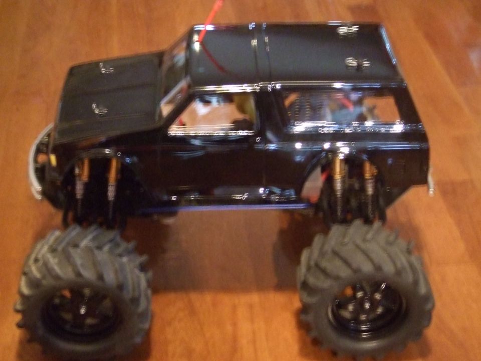 Black RC monster truck with large tires and visible suspension components on a wooden surface