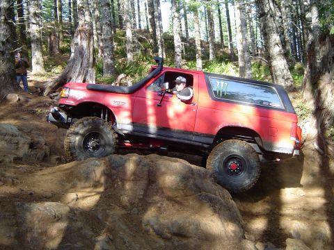 1989 Ford Bronco - A red 1989 Ford Bronco navigates a rocky trail in a forest setting.
