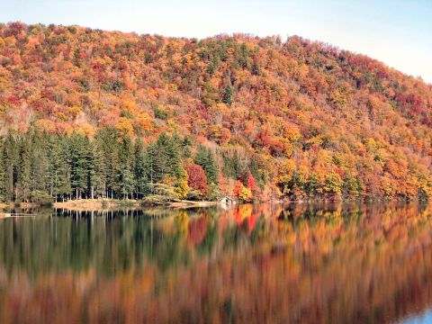 1985 Ford LTD Crown Victoria - A small boathouse is visible on the shore of a lake surrounded by trees in peak autumn color.