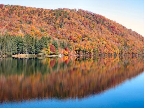 1985 Ford LTD Crown Victoria - A tranquil lake mirrors a hillside ablaze with the vibrant colors of fall foliage under a clear sky.