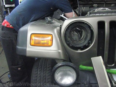 1987 Suzuki Samurai - A person works on the front end of a Jeep Wrangler, which is missing its driver's side headlight assembly.