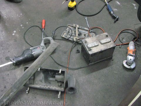 1987 Suzuki Samurai - Tools and a car battery are laid out on a workshop floor, suggesting vehicle maintenance or repair.