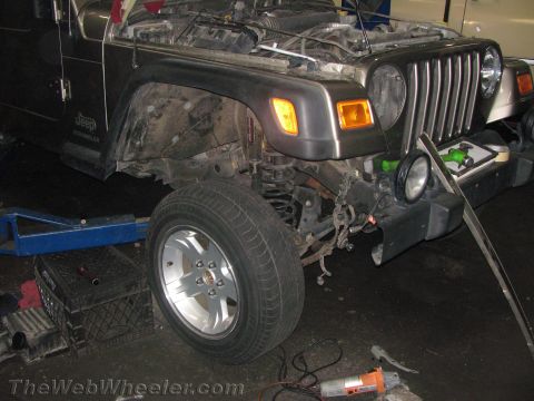1987 Suzuki Samurai - Front end of a Jeep Wrangler with the hood open, showing mechanical components and undergoing repairs.