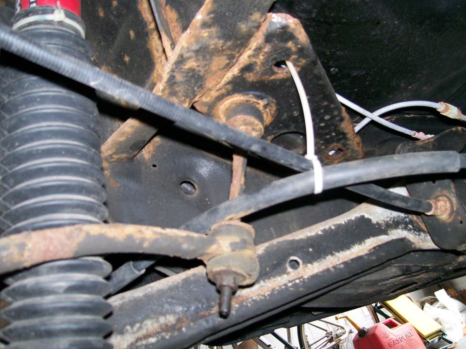 Underside view of rusty suspension parts, including a shock absorber and sway bar linkage