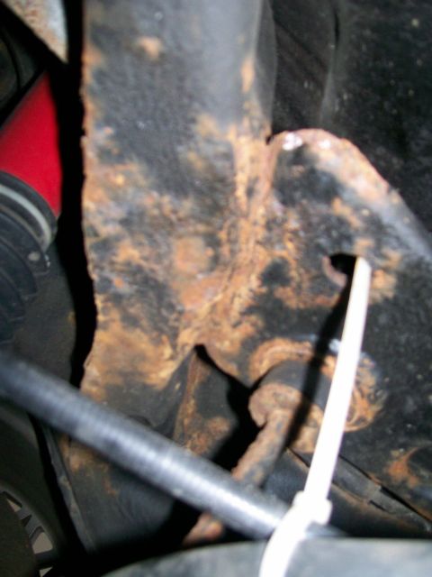 1995 Mercury Grand Marquis - Close-up of a heavily rusted suspension component, possibly a rear sway bar, with a red hose and black tubing visible.