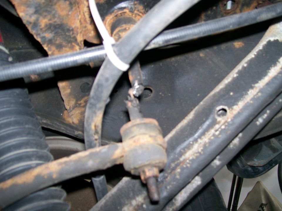 Close-up of rusty suspension parts, including a sway bar link and hoses, on a vehicle