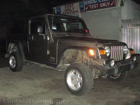 1987 Suzuki Samurai - A dark colored Jeep Wrangler is parked in front of a smog test station, showing damage to its front end.