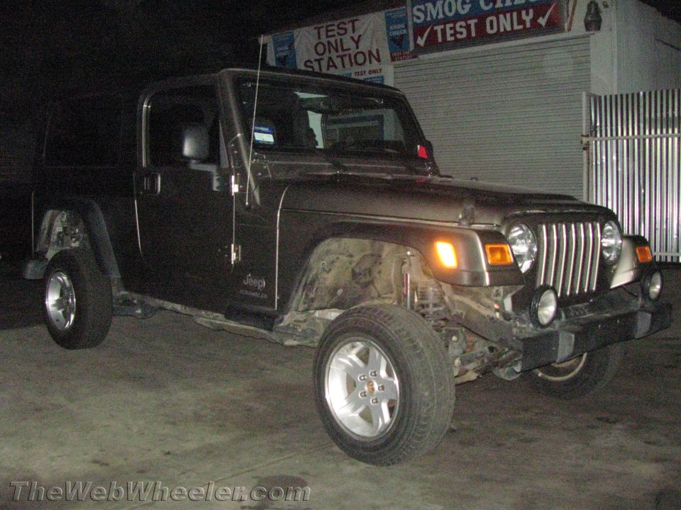 Dark Jeep Wrangler with front damage parked outside a smog test station