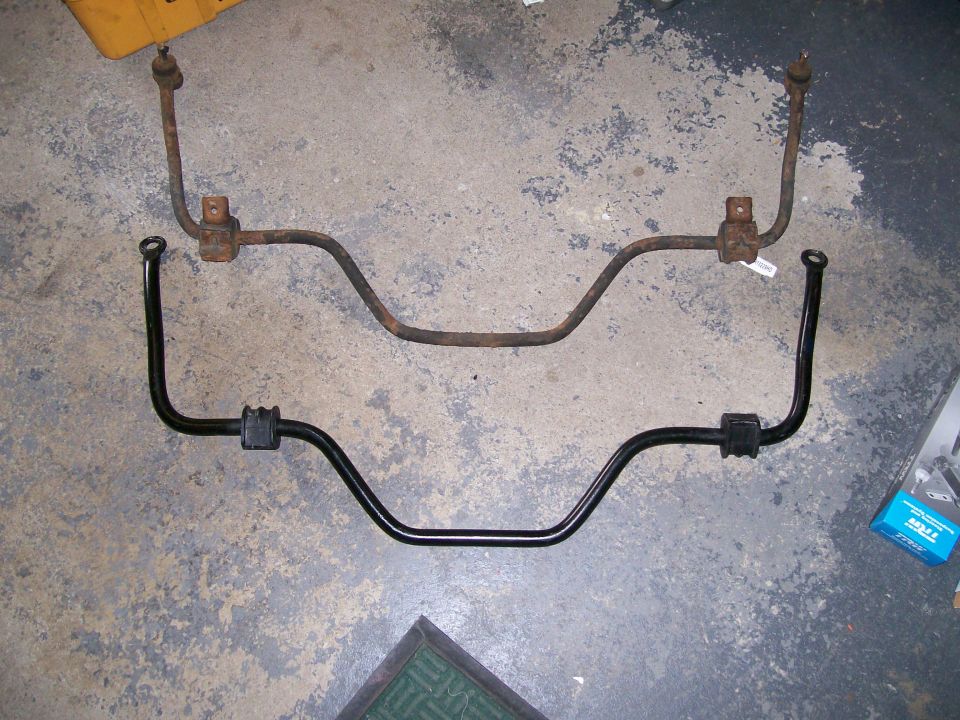 Rusty sway bar above a new black sway bar with rubber bushings