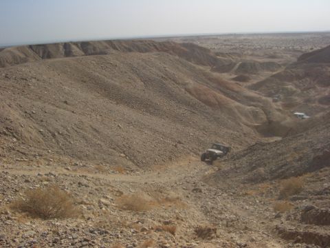 1985 Ford Bronco - Multiple off-road vehicles traverse a challenging, arid canyon terrain under a clear sky.