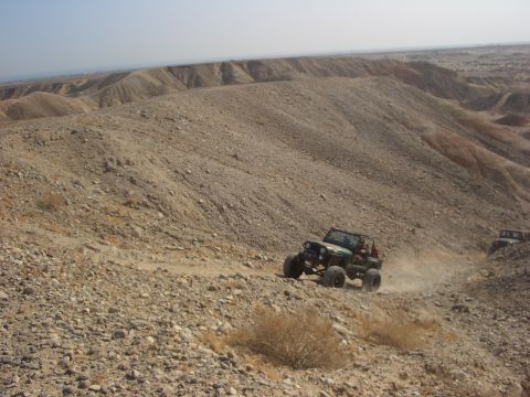 1985 Ford Bronco - Off-road vehicles navigate a challenging terrain in a barren, hilly desert environment.
