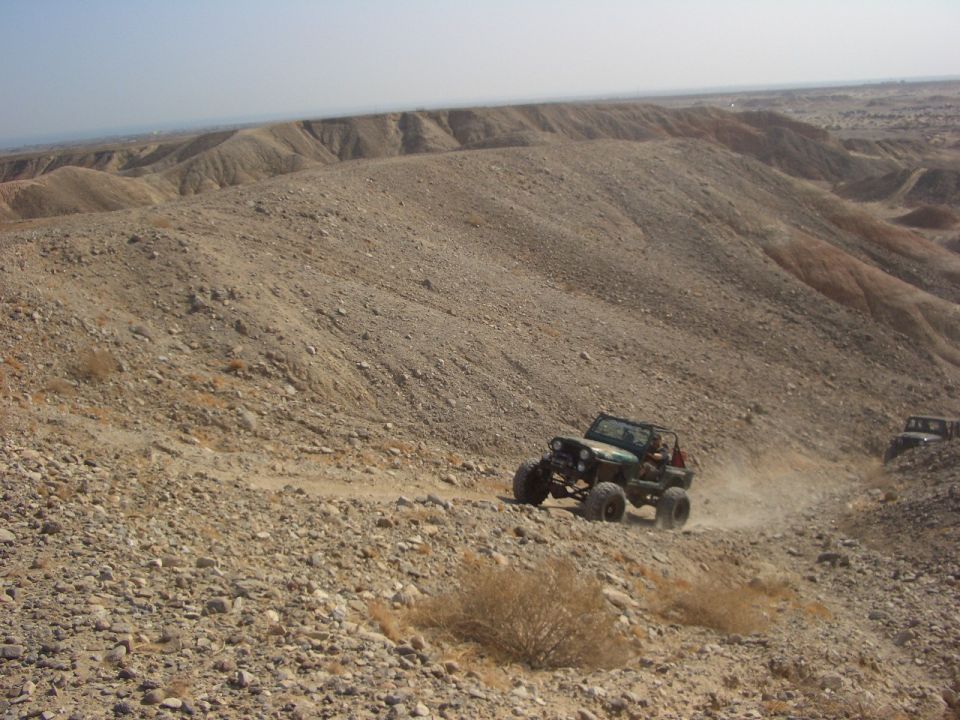 Two off-road vehicles descend a dusty, rocky slope in a desert landscape