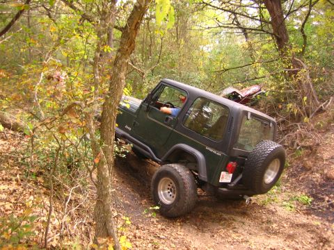 2001 Jeep Wrangler - A green Jeep Wrangler navigates a steep, wooded trail, with another vehicle visible in the background.