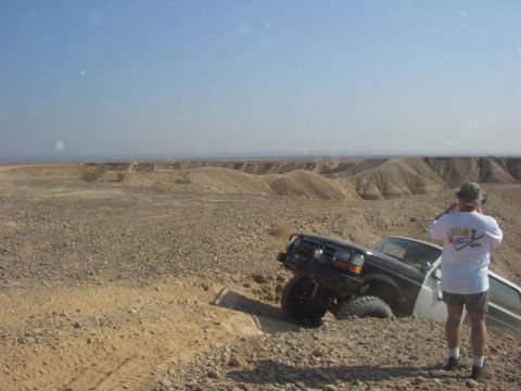 1985 Ford Bronco - A black SUV, likely a 1992 Ford Bronco, is stuck in a ditch while navigating a rocky desert terrain.