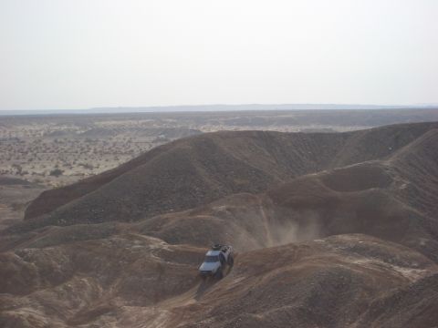 1985 Ford Bronco - A vehicle navigates a steep, dusty incline in a barren, hilly terrain under a clear sky.