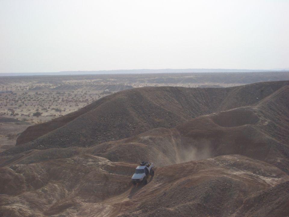 Off-road vehicle climbing a dusty hill in a desert landscape