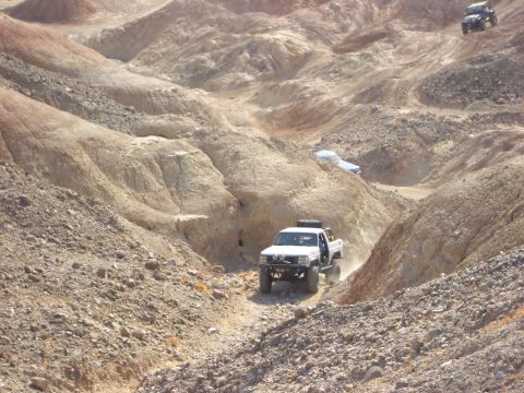 1985 Ford Bronco - Multiple off-road vehicles navigate a challenging, arid landscape with steep, eroded hillsides.