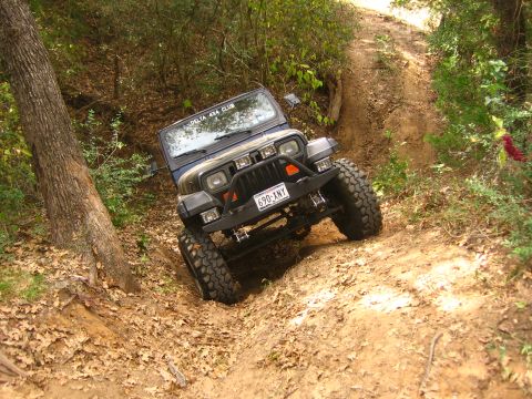 2001 Jeep Wrangler - A blue Jeep Wrangler navigates a challenging off-road trail, its tires gripping the loose dirt.